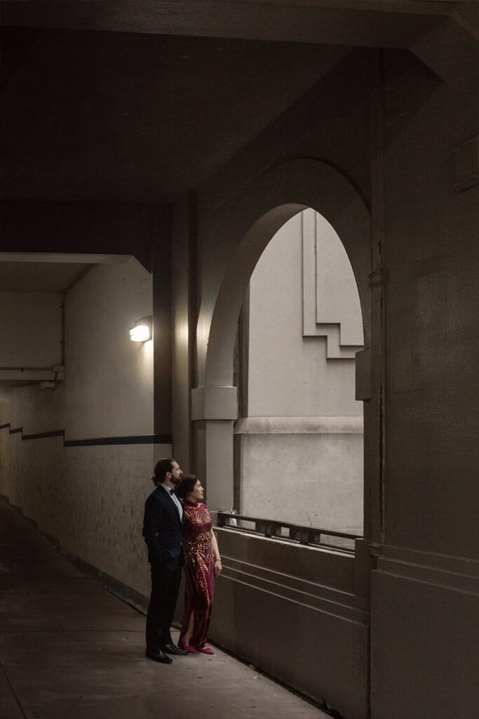 A woman in a red dress and a man in a suit standing together in an urban underpass at night.