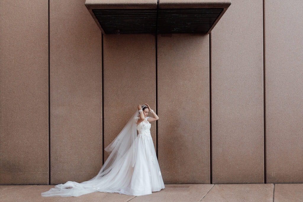 Elegant bride in white wedding dress standing against modern brown wall, minimalist wedding photogra.