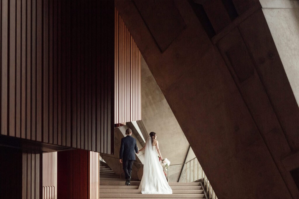 A bride and groom walking up modern architectural stairs in a contemporary building.
